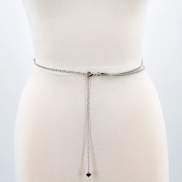 A silver metal belt made of two parallel cable style chains. Seen on a dress form from behind to show the lobster clasp style enclosure and heart-shaped charm