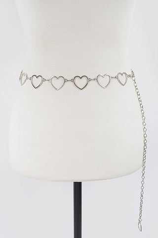 A shiny silver chain belt with metal hearts connecting each link. There is a silver heart charm at the end of the chain. The belt is shown on a mannequin torso