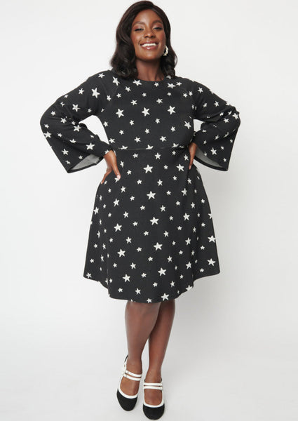 A black sweater knit fit and flare dress with raglan bell sleeves in a black and white star pattern. Shown on a model with their hands on their hips