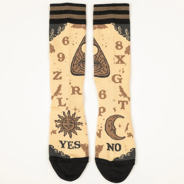 A pair of unisex crew socks with a spirit board design. Each pair has a beige background with dark brown heels and toes & a striped cuff of two shades of brown. Each sock has corresponding designs that when put together resemble the full markings of a spirit board including planchette. This shows the front view with both socks next to each other 