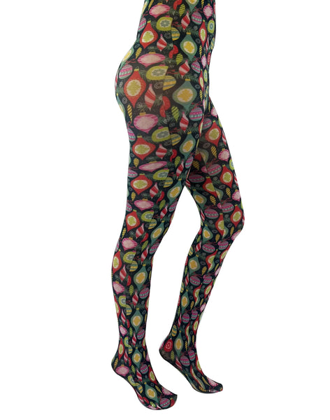 vibrantly colored novelty tights featuring assorted vintage style Christmas ornaments, snowflakes, and evergreen branches against a black background, shown on model