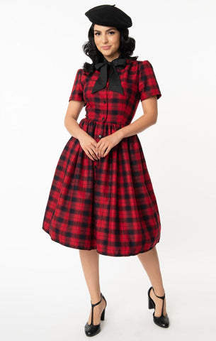 Cora Dress in rich red & black plaid features front button closure, fit & flare silhouette with gathered skirt in a just below the knee length, short puff shoulder sleeves, side seam pockets, and a black tie-closure collar. Shown on model.