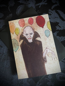 A rectangular birthday card of a watercolor illustration of a white vampire surrounded by colorful balloons