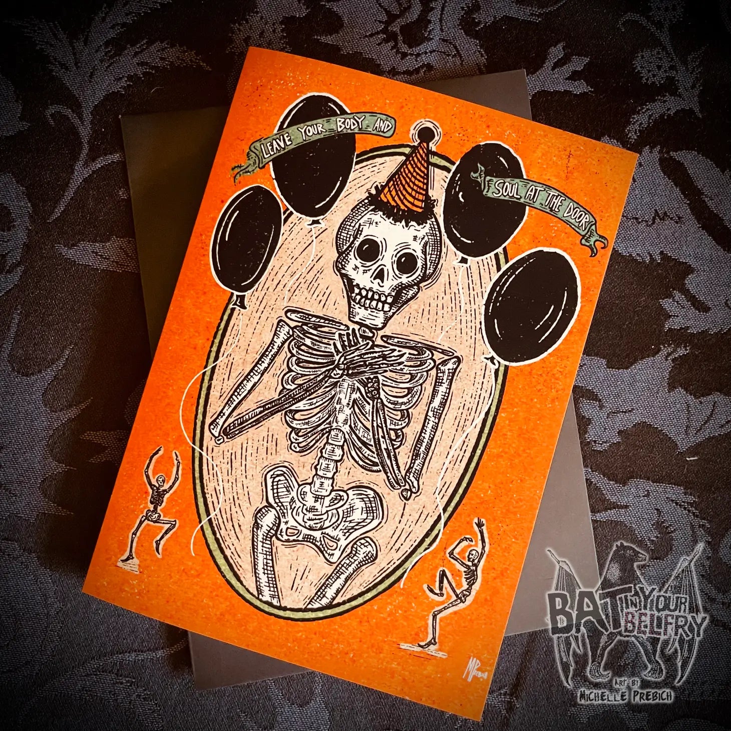 A birthday card with an illustration of a skeleton wearing an orange and black party hat surrounded by black balloons with the message “Leave your body and soul at the door”. There are two small dancing skeletons at the bottom of the card in front of an orange background