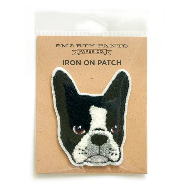 A chenille patch of a black and white Boston Terrier dog in front of brown cardboard packaging. The words “Smarty Pants Paper Co.” are written on the cardboard