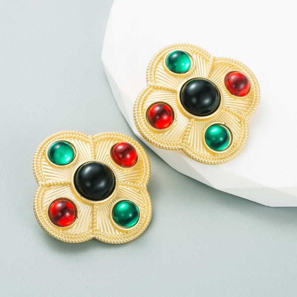 Stylized clover shaped statement post earrings in a matte textured gold metal with one large black rhinestone surrounded by red and green smaller rhinestones 