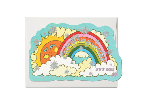 Die cut greeting card of a smiling sun surrounded by a rainbow and clouds. Lettering says “Everything Sucks But You” in script. Star details and lettering are silver holographic foil
