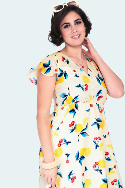 yellow background cherry lemonade print dress with v-neckline, covered button detail on the fitted bodice, short flutter sleeves, self belt, comfortable elasticized front waist seam, and flared below the knee length, shown on model