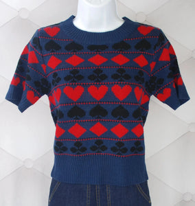 Acrylic pullover sweater with allover knit-in pattern of hearts, diamonds, spades, and clubs in red and black on a dark blue background. Ribbed collar and hems on sleeves and bottom of sweater.