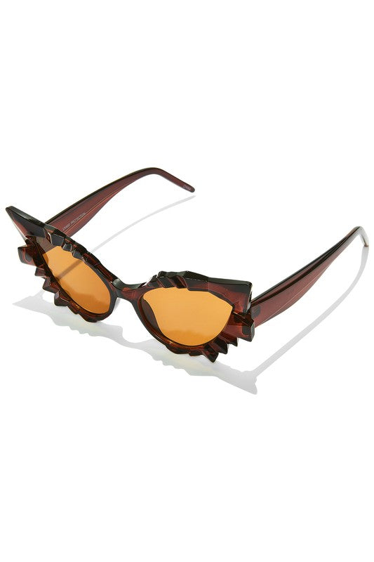 A pair of cat-eye sunglasses sitting at a 45 degree angle. They are a translucent warm brown color with geometric detail above and below the lenses,which are brown
