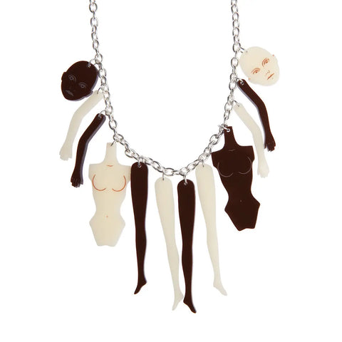 A necklace made of a silver link style chain with various disembodied doll parts- heads, arms, legs, torsos- in both off-white and dark brown- with details etched into the faces and torsos.