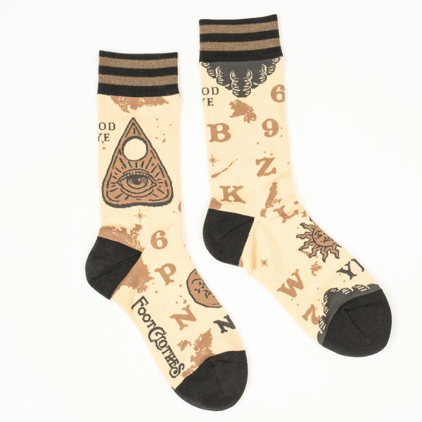 A pair of unisex crew socks with a spirit board design. Each pair has a beige background with dark brown heels and toes & a striped cuff of two shades of brown. Each sock has corresponding designs that when put together resemble the full markings of a spirit board including planchette 