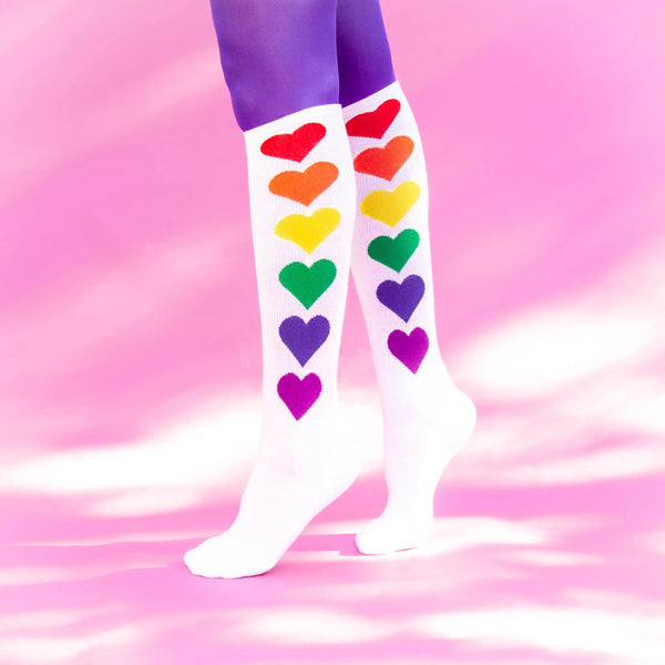 A pair of legs wearing purple tights with the rainbow heart knee socks overtop.