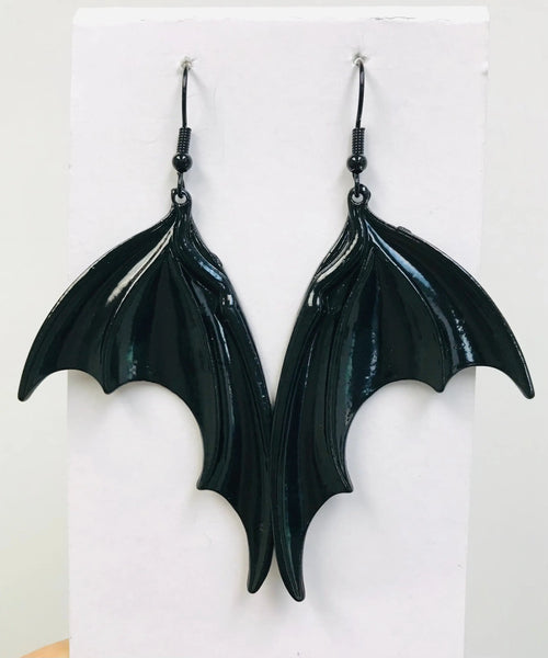 A pair of dangle earrings with a black enameled metal bat wing charm on each earring 