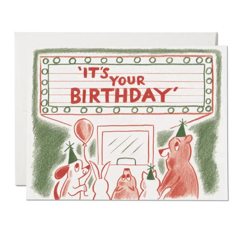 A heavyweight card stock offset printed note card with an illustration by Nicholas John Frith of some party animals in front of an old-fashioned movie theatre marquee. Marquee has the caption “It’s Your Birthday” and illustration is done in pencil crayon in shades of red and green