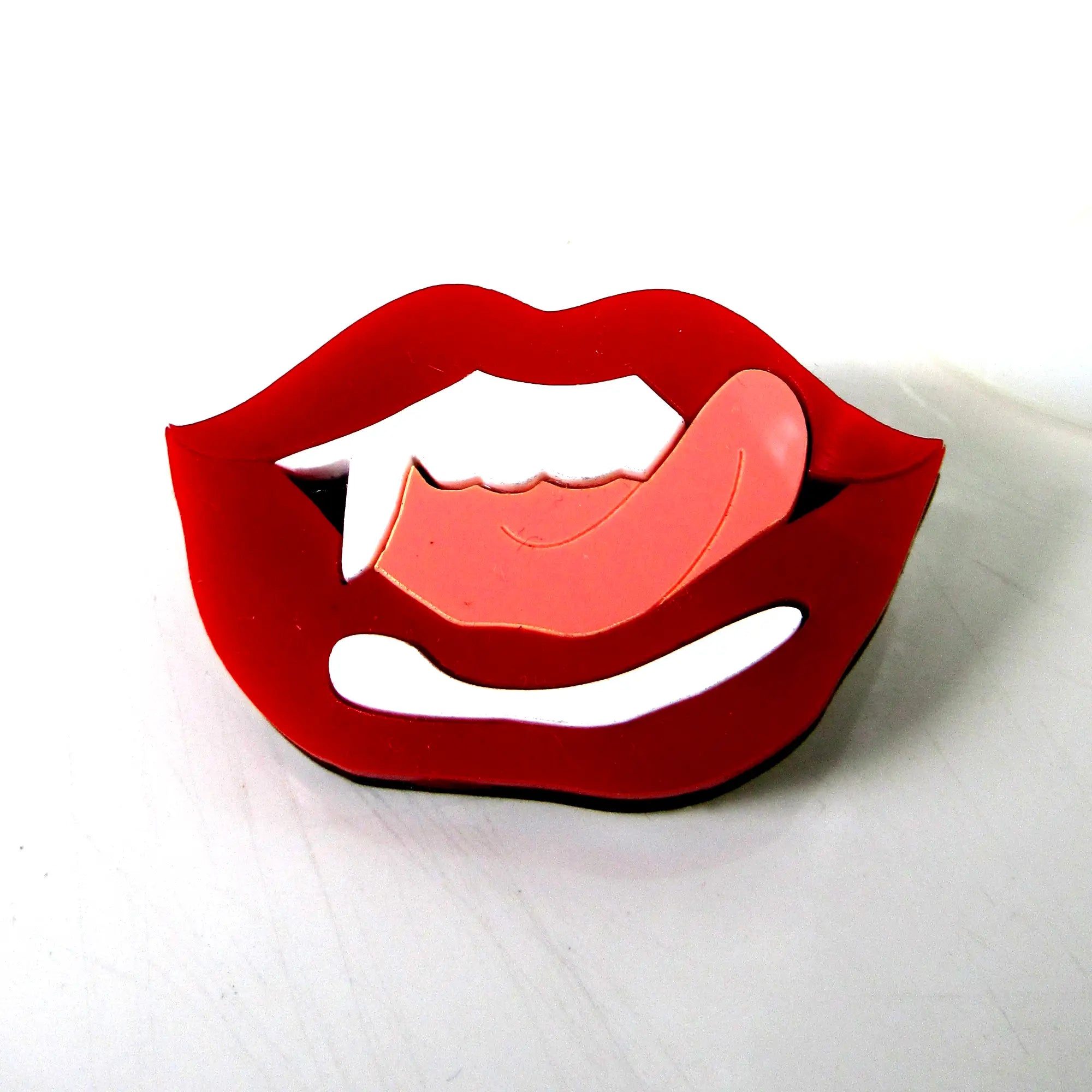 A laser cut layered acrylic brooch of a vampire’s mouth with bared fangs and tongue sticking out