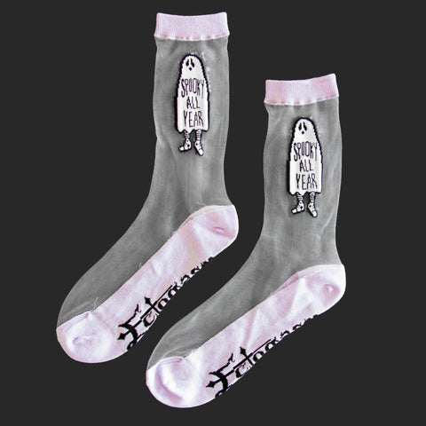 A pair of crew socks with a pale purple cuff, toe, and heel with the image of a ghost with the words “SPOOKY ALL YEAR” written on the middle of the ghost’s sheet. The brand name Ectogasm is written on the bottom of the sock 