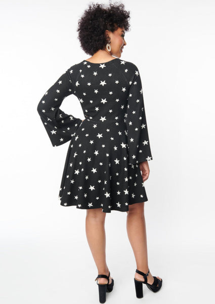 A black sweater knit fit and flare dress with raglan bell sleeves in a black and white star pattern. Back of dress shown on a model