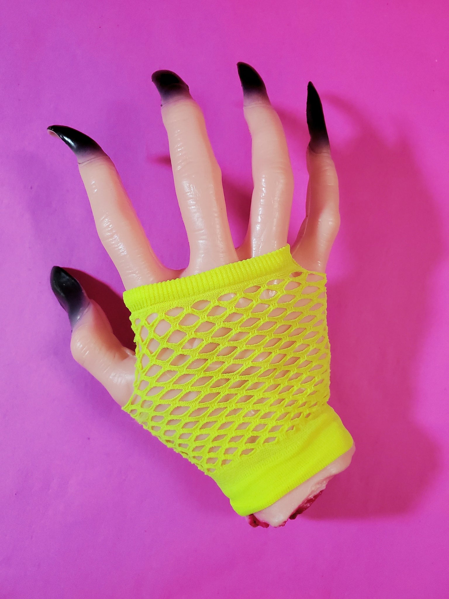 Wrist-length bright neon yellow fingerless fishnet glove, shown on halloween prop hand