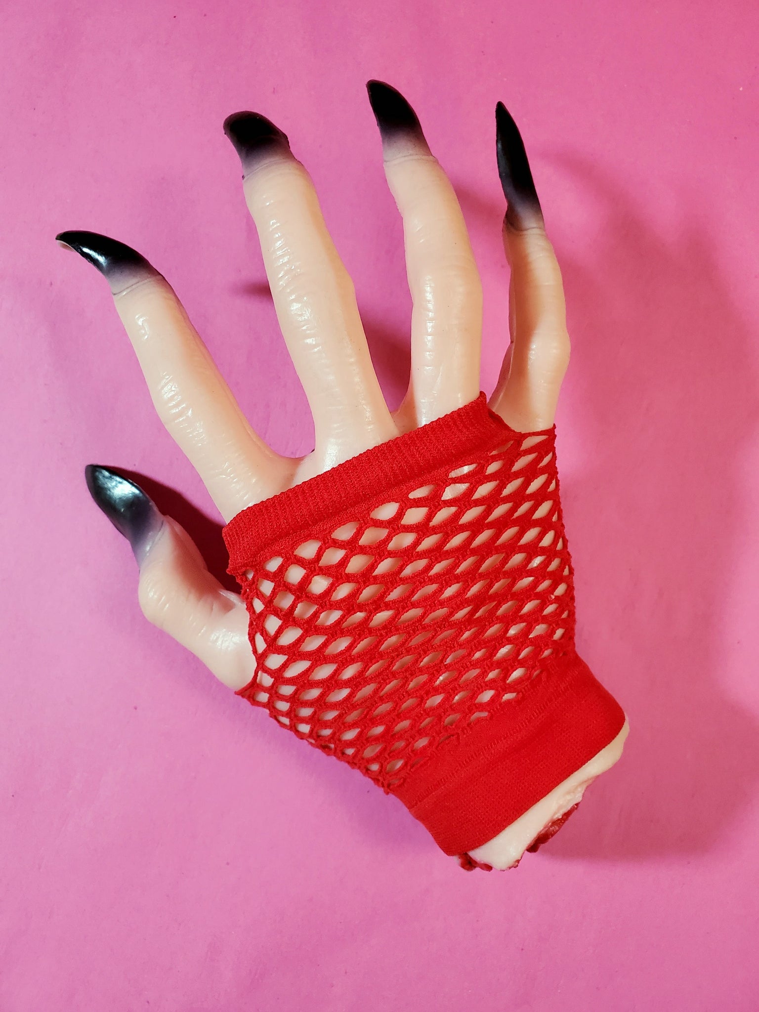 Wrist-length bright red fingerless fishnet glove, shown on halloween prop hand