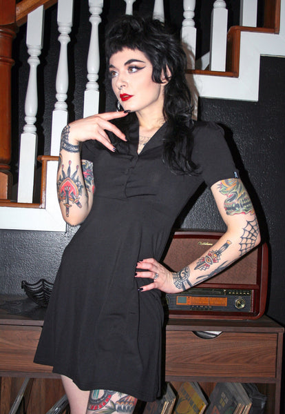 A model wearing a black diner style button up dress with puffed short sleeves