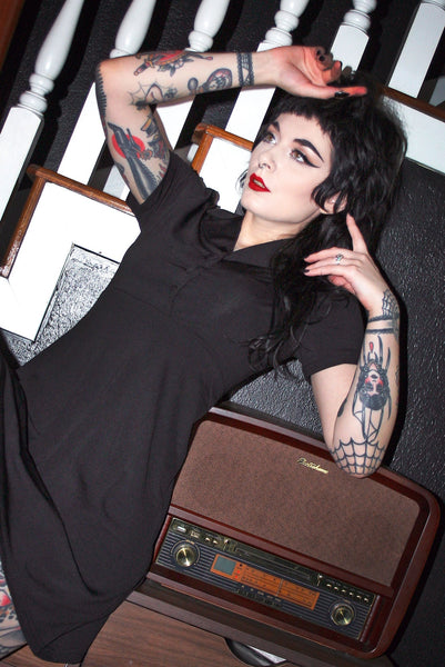 A model wearing a black diner style button up dress with puffed short sleeves