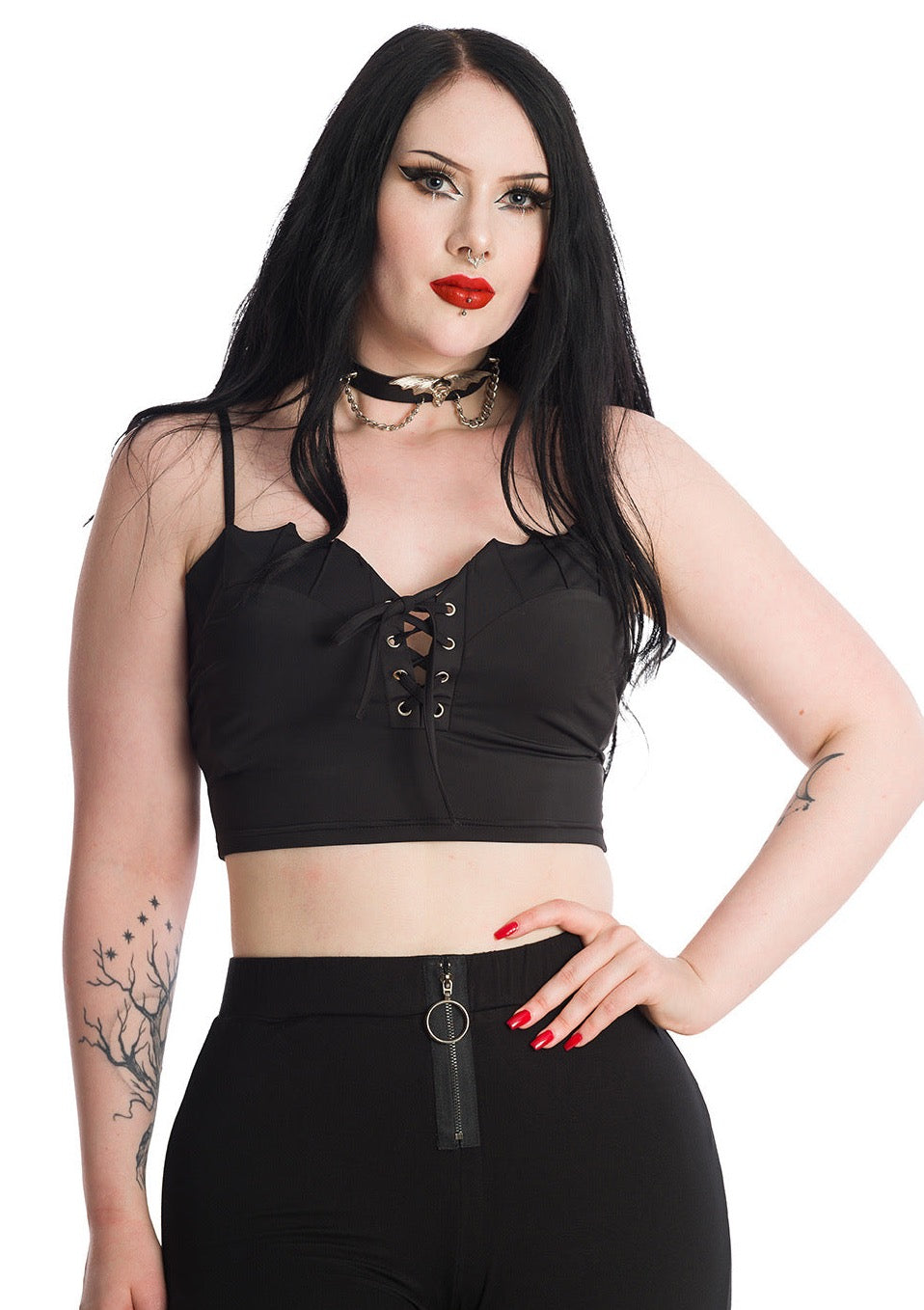 A model wearing a black bustier style crop top with a sweetheart neckline with batwing-style scalloped detail at the top of the bodice, 4 rows of lace-up eyelets with silver metal hardware, and adjustable spaghetti straps. Shown from the front