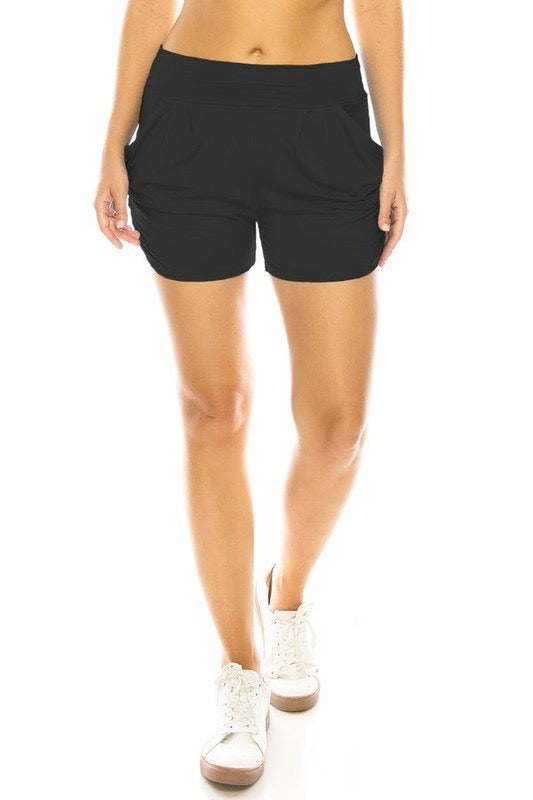 A model wearing black knit shorts with elastic waist band, pleated front, ruched side seam detail, and pockets. Seen from front