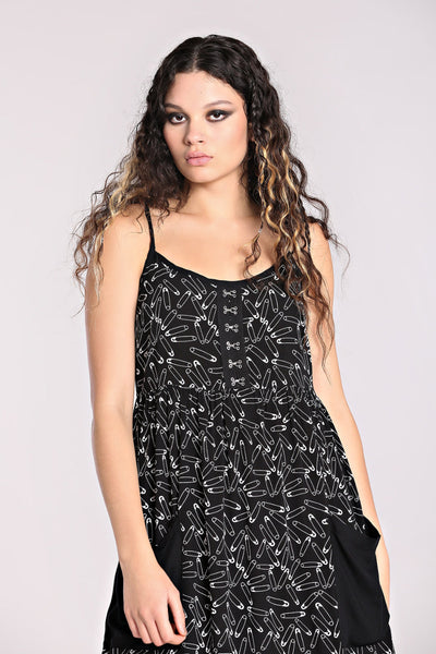 model wearing a black sleeveless sundress with an all-over white safety pin pattern. The dress has black spaghetti straps and silver metal hook and eye detail at the bodice. The skirt is midi length with two black patch pockets at the hips. Seen in close up