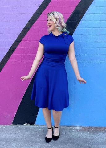 1940s inspired royal blue stretch knit Bombshell Dress side tie at the neck, ruched waist, flared knee length skirt, shown on model