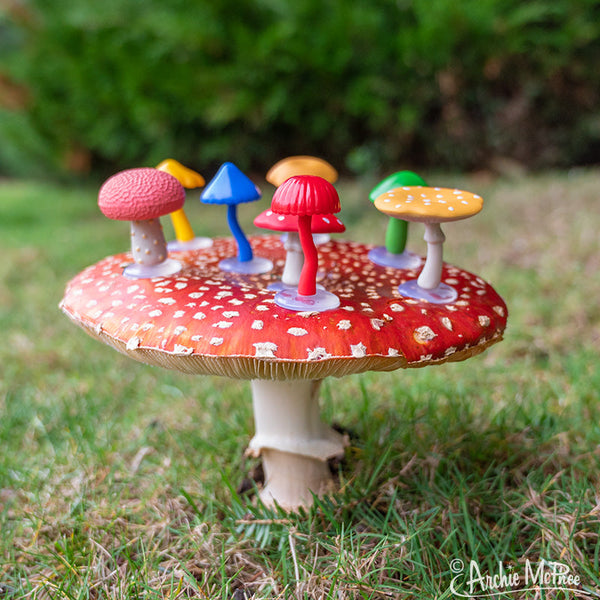 colorful collection of eight different soft vinyl mini mushrooms, pictured displayed outdoors on an amanita muscaria toadstool mushroom