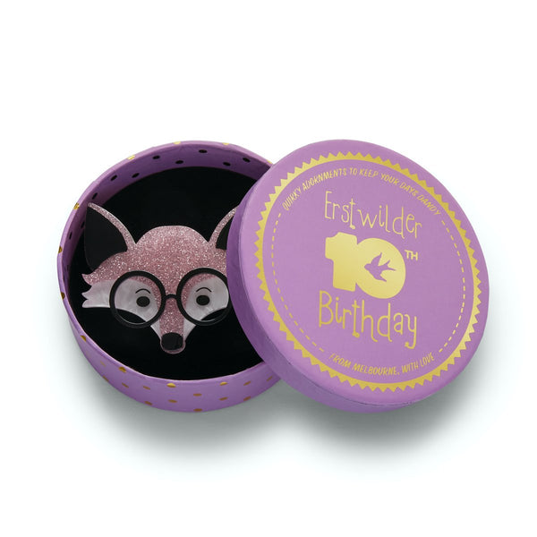 pale pink glitter, black, and white glasses-wearing fox face layered resin brooch, shown in illustrated round box packaging