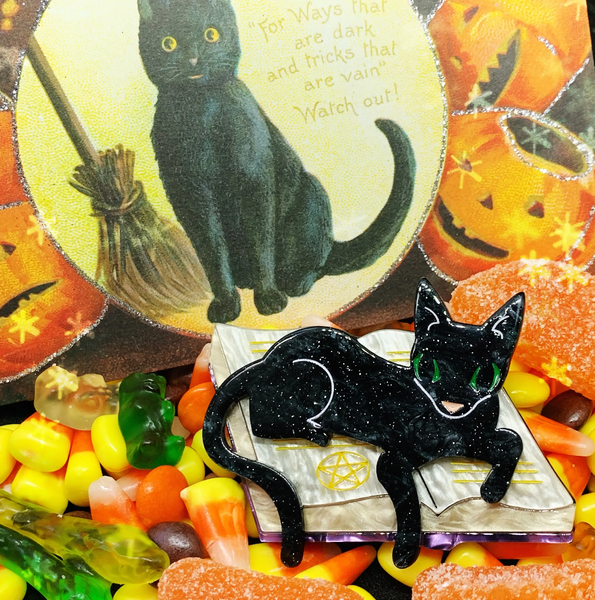 "Furmiliar Pywacket" glittery black green-eyed cat lounging on a witch's book of spells layered laser cut resin brooch