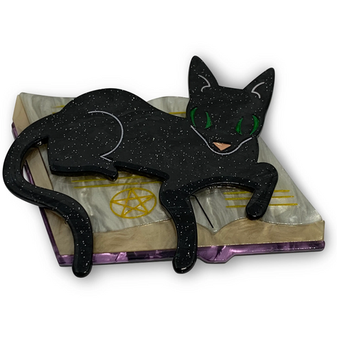 "Furmiliar Pywacket" glittery black green-eyed cat lounging on a witch's book of spells layered laser cut resin brooch