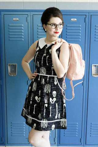 sleeveless "Anatomically Correct" Dress from Retrolicious features a black background allover off-white glow-in-the-dark print of scientifically labeled human skeleton parts with contrast white pointed collar & piping details, shown on model