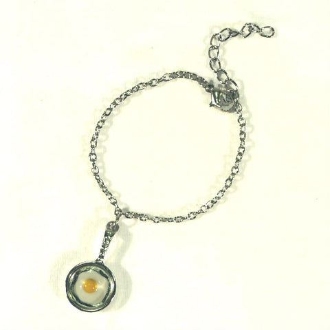 enameled white and yellow Fried Egg in a shiny silver metal frying pan charm on a silver metal chain bracelet