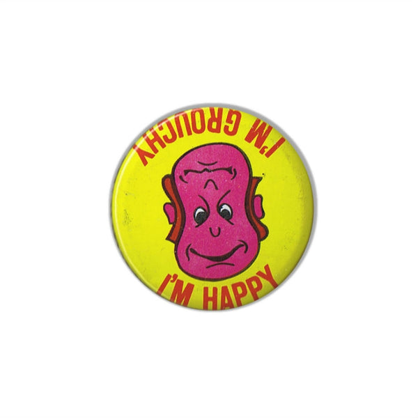 1.5" round metal vintage 1970s deadstock button that can be spun around to either show a frowning "I'M GROUCHY" guy's face or a smiling "I'M HAPPY" one