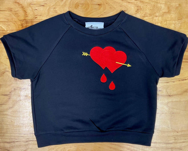 cropped length thick black cotton short sleeve raglan pullover top featuring an embroidered bold red pair of bleeding hearts pirced by a bright yellow arrow, shown flatlay