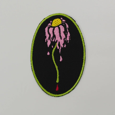 wilted pink daisy with blood drip on black canvas oval embroidered patch with green border