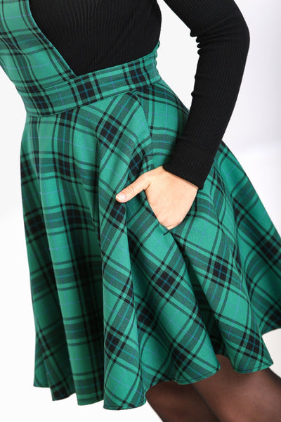 green and black plaid pinafore dress with crossover straps, front button closure, nipped in waist, and flared above the knee length skirt, styled with black turtleneck, shown on model
