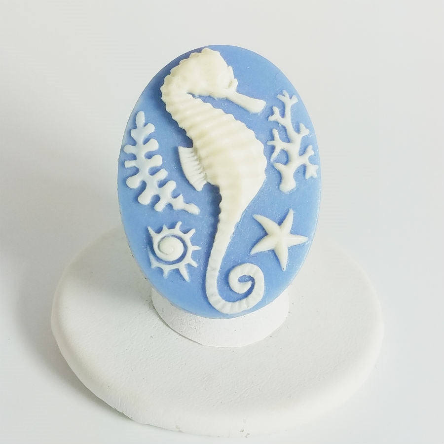 Cameo style creamy white seahorse in relief on a blue oval with adjustable clear glass bead stretch band ring