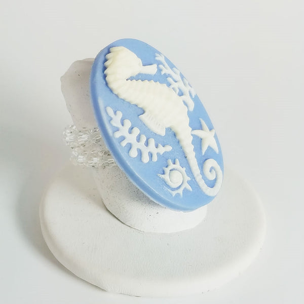 Cameo style creamy white seahorse in relief on a blue oval with adjustable clear glass bead stretch band ring