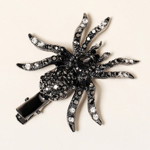 A spider-shaped alligator style hair clip in a gunmetal color decorated with black and clear rhinestones and a large black jewel on the spider's head. Front of clip is shown