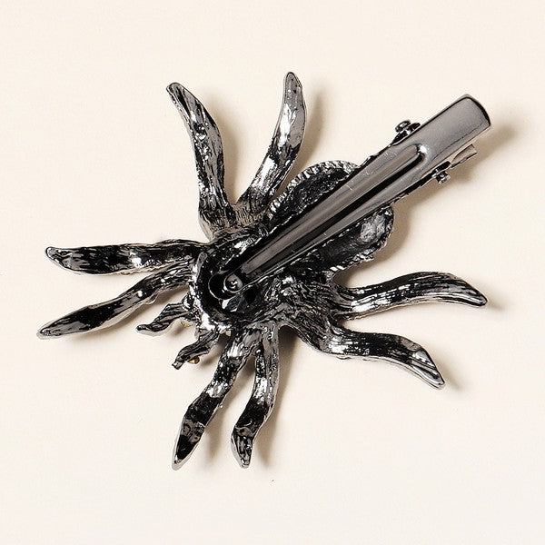 A spider-shaped alligator style hair clip in a gunmetal color decorated with black and clear rhinestones and a large black jewel on the spider's head. Back of clip is shown