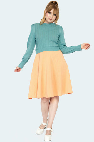 A model wearing a long sleeved pullover sweater in a robin’s egg blue color. It has a pointelle chevron style geometric pattern knitted into the front of the front of the sweater, slightly puffed shoulders with pleated detail and a ribbed jewel style neckline with matching wide ribbed cuffs