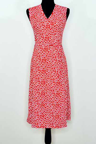 A dress form with a sleeveless knee-length wrap dress in a pattern of white scattered dots on a red background. Shown from the front 