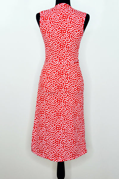 A dress form with a sleeveless knee-length wrap dress in a pattern of white scattered dots on a red background. Shown from the back