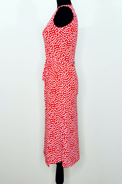 A dress form with a sleeveless knee-length wrap dress in a pattern of white scattered dots on a red background. Shown from the left side