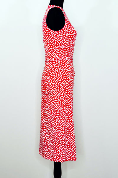 A dress form with a sleeveless knee-length wrap dress in a pattern of white scattered dots on a red background. Shown from the right side