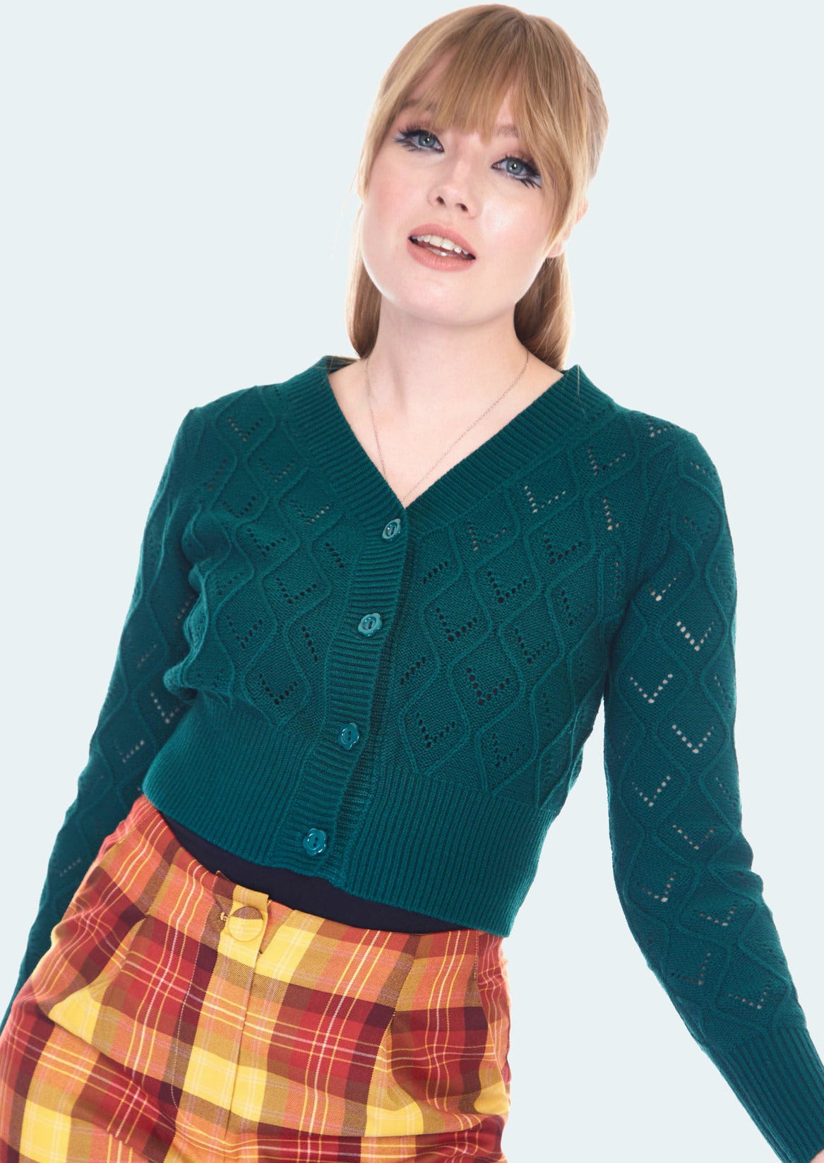 A model wearing a dark teal knit-in openwork cardigan with matching dark teal flower shaped buttons. It is slightly cropped and has a shallow v-neck